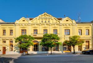 un gran edificio amarillo con árboles delante de él en Hotel Golden Eagle, en Levice