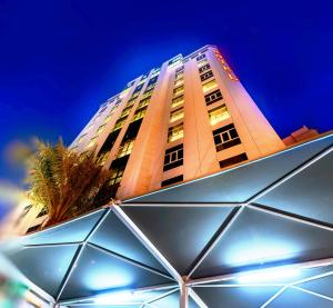 ein hohes Gebäude mit einer Palme davor in der Unterkunft Bravo Royal Hotel Suites in Kuwait