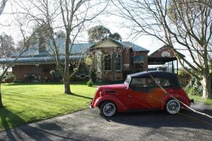 an old red car parked in front of a house at Butterfly Farm Bed and Breakfast Nirranda in Nirranda