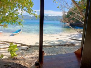 una finestra con vista su una spiaggia con una barca in acqua di I&D Home Stay Raja Ampat a Yennanas Besir