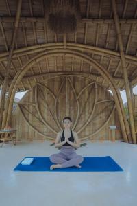 una mujer sentada en una esterilla de yoga azul en una habitación en Wasita Eco Villa Ubud, en Ubud