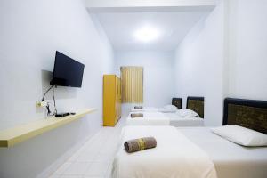 um quarto de hotel com três camas e uma televisão de ecrã plano em Marcello Residence Siwalankerto near Petra University Surabaya Mitra RedDoorz em Surabaya