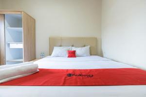 een slaapkamer met een wit bed en een rood kussen bij RedDoorz at Osuko Residence Sukomanunggal Jaya in Surabaya