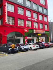 een man voor een rood gebouw met geparkeerde auto's bij MRC Hotel Melaka Raya in Melaka