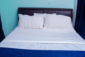 - un lit avec des draps et des oreillers blancs dans l'établissement Cozy Residences, à Kampala