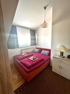 Cama roja en una habitación pequeña con ventana en Apartman Anita, en Varaždin