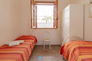 two beds in a room with a window and a chair at Orsetta Flat - Torre Dell'Orso in Torre dell'Orso