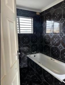 a black tiled bathroom with a tub and a window at Wood Road Apartments in Durban