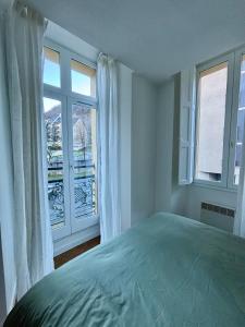 um quarto com uma cama e uma grande janela em Appartement au centre-ville à 100 m des télécabines avec parking souterrain gratuit em Luchon