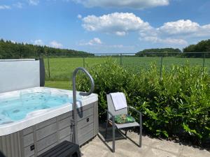 a hot tub and a chair in front of a field at Summio Villaparc Schoonhovenseland in Hollandscheveld