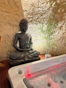 a statue of a buddha sitting next to a tub at Hôtel-Restaurant-Chambre Insolite Spa - Le XII de Luynes in Luynes