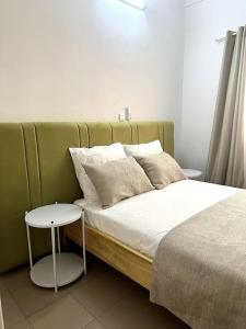 uma cama com uma cabeceira verde com uma mesa lateral em Appartement - Le Grège em Ouagadougou