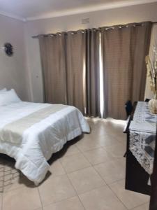 a bedroom with a bed and a desk and curtains at Mimosa's @ 44 in Roodepoort
