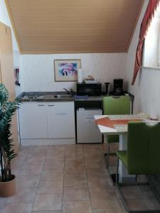 Apartment in Stauseenähe في Rainau: مطبخ مع دواليب بيضاء وطاولة مع كراسي خضراء