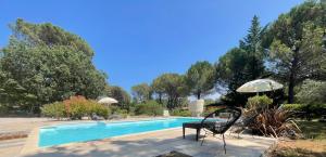a swimming pool with two chairs and an umbrella at La maison de la Cigale in Forcalqueiret