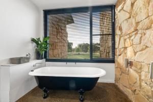 a bath tub in a bathroom with a stone wall at Unique and Modern Farm Stay with Pool and Foosball and Yard in Buninyong
