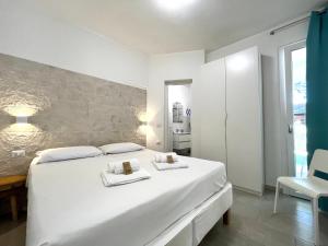 een witte slaapkamer met een groot wit bed en 2 handdoeken bij Angolo Mare Apartments & Rooms in Porto Pino