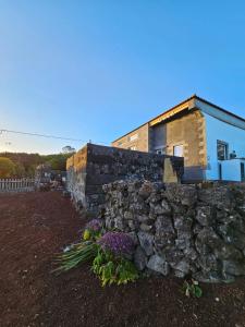 a stone wall in front of a house with flowers at Waka Waka Pico Azores in Cais do Pico