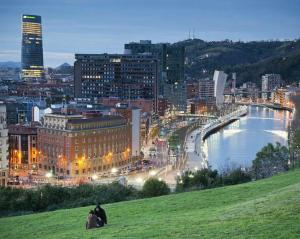 Ein Paar, das nachts auf einem Hügel mit Blick auf eine Stadt sitzt in der Unterkunft The Park House II by homebilbao. in Bilbao