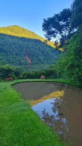 a pond in the grass next to a hill at Cabana valle Pietra Hospedagem sofisticada em Nova Petrópolis in Nova Petrópolis