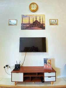 een flatscreen-tv op een witte muur met een klok bij WawAmir Homestay @ Seri Iskandar in Seri Iskandar