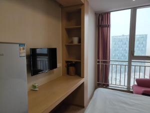 Yangzhou Xianyun Apartment في يانغتشو: غرفة مع تلفزيون وشرفة مع سرير