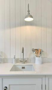 a white kitchen with a sink and a light at Grange Barn, Ashford In The Water in Great Longstone