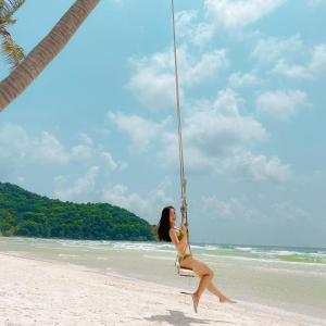 Una donna in bikini seduta su un'altalena sulla spiaggia di Agarwood Boutique House Phu Quoc - Free Kitchen a Phu Quoc