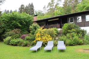 un grupo de sillas sentadas en el césped frente a una casa en Ferienhaus Naturliebe 6000qm Parkgarten am Wald, umzäunt, Kamin, Sauna, en Laubach