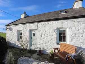 a white stone cottage with a bench in front of it at Pant y Crintach in Amlwch