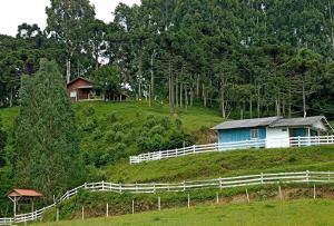 Ein blaues Haus auf einem Hügel mit einem weißen Zaun in der Unterkunft Pousada Vale do Tigre in Rio Rufino