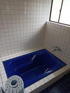 a blue tub in a white tiled bathroom at Minshuku Kamagari in Kure