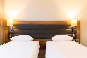 two beds in a hotel room with white sheets at Moxy London Excel in London