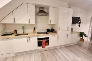 een witte keuken met witte kasten en een houten vloer bij Luxurious Ensuite in Edgware