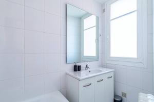 W białej łazience znajduje się umywalka i lustro. w obiekcie Agréable appartement près de la capitale w mieście Neuilly-sur-Seine