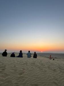 eine Gruppe von Menschen, die am Strand sitzen und den Sonnenuntergang beobachten in der Unterkunft Hostel Desert Home Stay in Jaisalmer