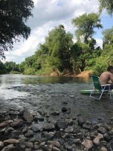 un hombre sentado en una silla junto a un río en Pousada da Lua, en Rolante