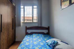 a bedroom with a bed with a blue comforter and a window at Apto c otima localizacao em Gloria, Belo Horizonte in Belo Horizonte