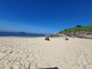 a group of people sitting on a sandy beach at Apartamento 2 suítes Frente à Praia de Camboinhas - Niterói - RJ - Brasil in Niterói