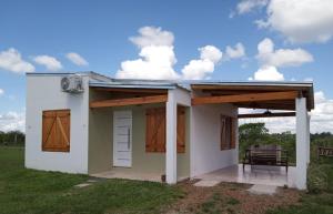 una pequeña casa blanca con toldo y un banco en "AGUAPÉ" Alojamiento rural con PILETA en Chajarí
