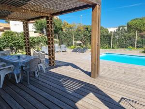 een houten terras met een tafel en stoelen naast een zwembad bij Bel appartement avec piscine privative à 150m de la plage 6 couchages in Le Barcarès