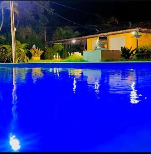 une piscine bleue avec une maison en arrière-plan dans l'établissement Chácara Nascimento, à Vitória de Santo Antão