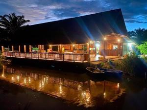 a house with a boat in the water at night at ปารมีฟาร์มสเตย์ in Ban Chao Nam