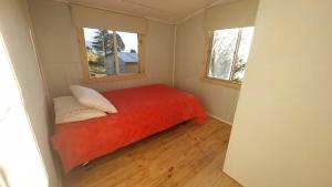 a small bedroom with a red bed with two windows at Cabaña Frente Al mar, Carretera Austral km 38,6, Puerto Montt in Puerto Montt