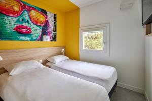 シュノーヴにあるKyriad Direct Dijon Sud - Chenoveの壁に絵画が飾られた部屋のベッド2台