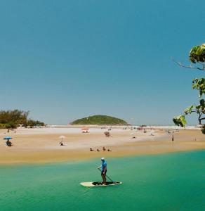 a man standing on a surfboard in the water at a beach at Kahuma in Imbituba +2 photos