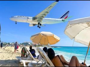 a plane flying over a beach with people sitting on chairs at Paradise in Caraibes in Cupecoy