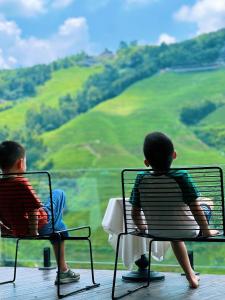 dos chicos sentados en sillas mirando las colinas en Beauty Lost Guest House龙胜龙脊梯田店, en Longsheng