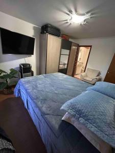 Schlafzimmer mit einem blauen Bett und einem Flachbild-TV in der Unterkunft Apartamento Central COM 02 BOX de garagem in Caxias do Sul