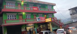 達旺鎮的住宿－Aajanta，一座绿色和红色的建筑,前面有汽车停放